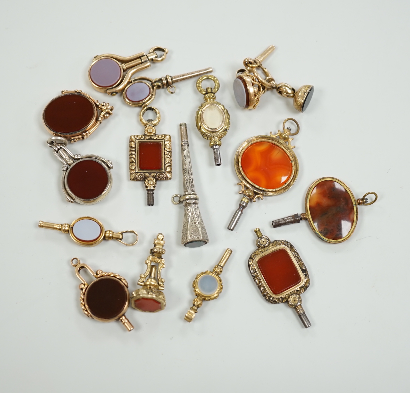 Sixteen assorted 19th century and later, 9ct gold and yellow or white metal overlaid and chalcedony set watch keys, including bloodstone, sardonyx, banded agate and moss agate and spinning fobs, largest 56mm.